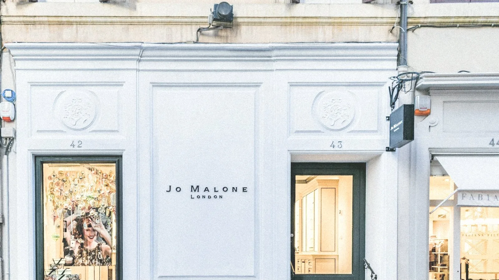 Fachada blanca de una boutique con molduras y escaparate iluminado