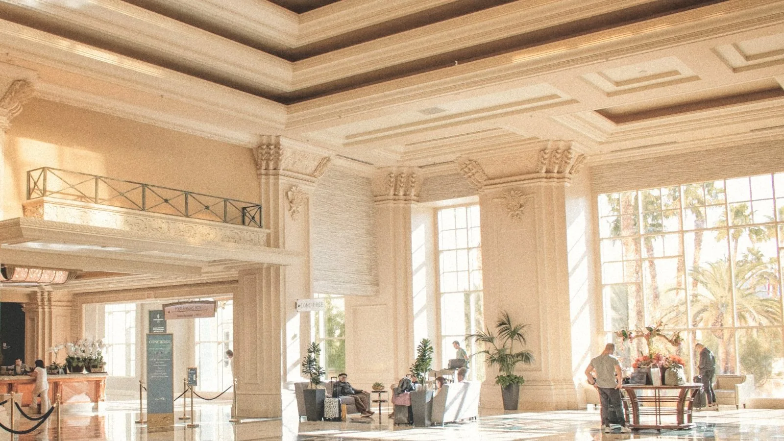 Vestíbulo de un gran hotel con columnas, ventanales y luz de tarde